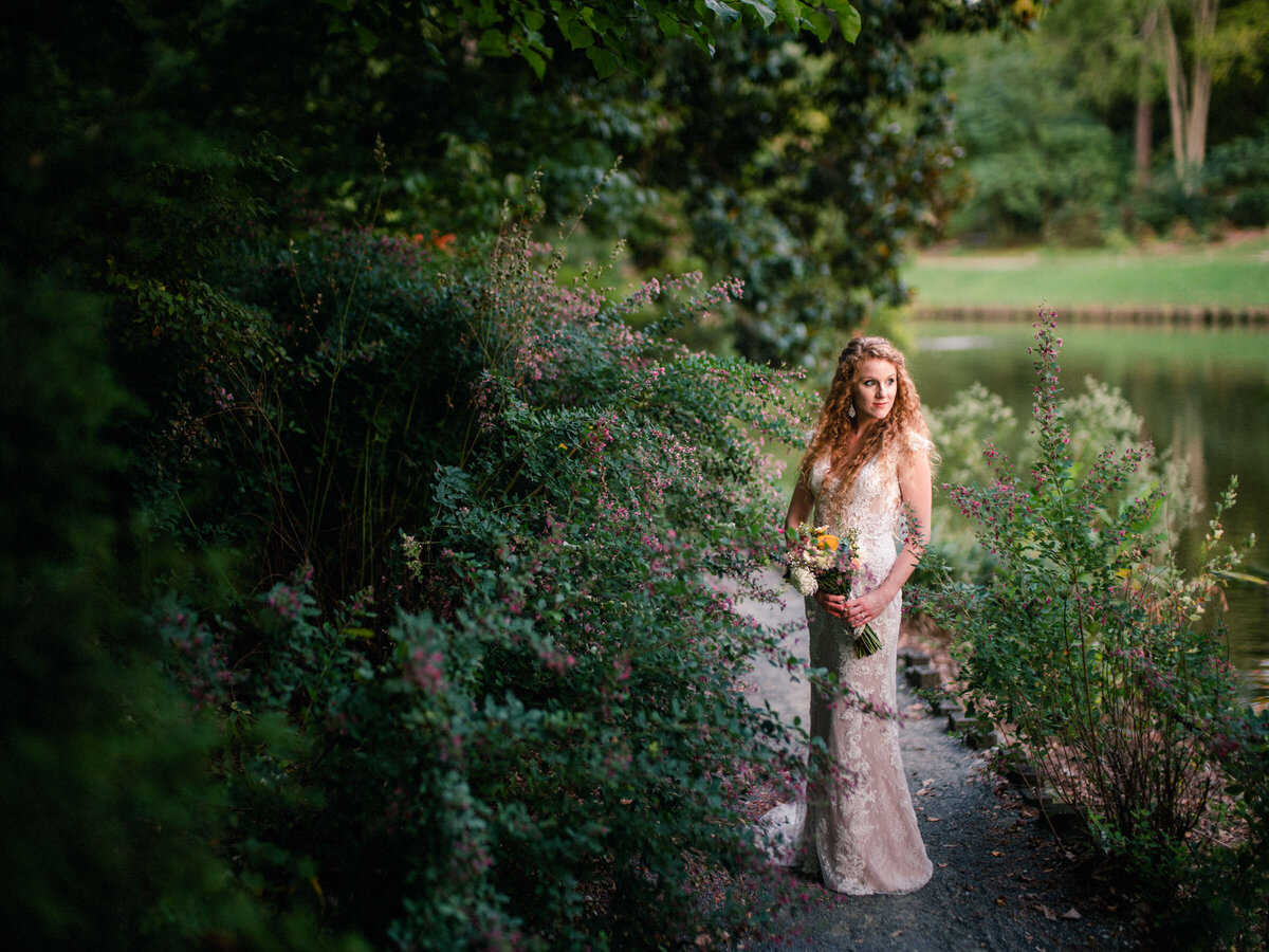 A bride holding a bouquet standing on a small path by a lake
