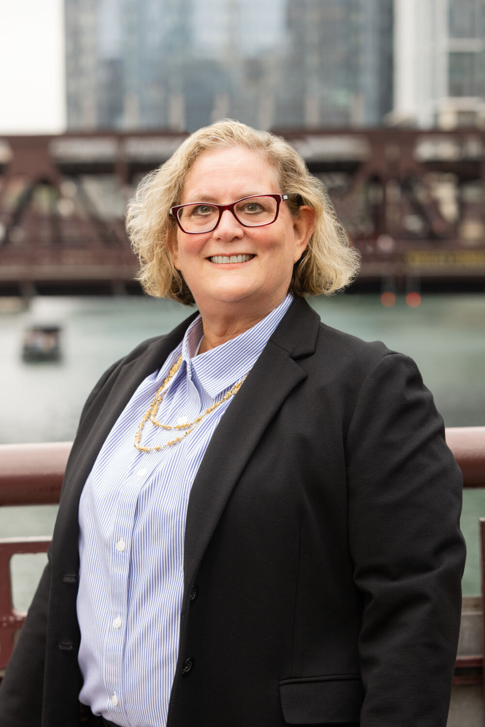 Woman in blazer and glasses standing on bridge with city view
