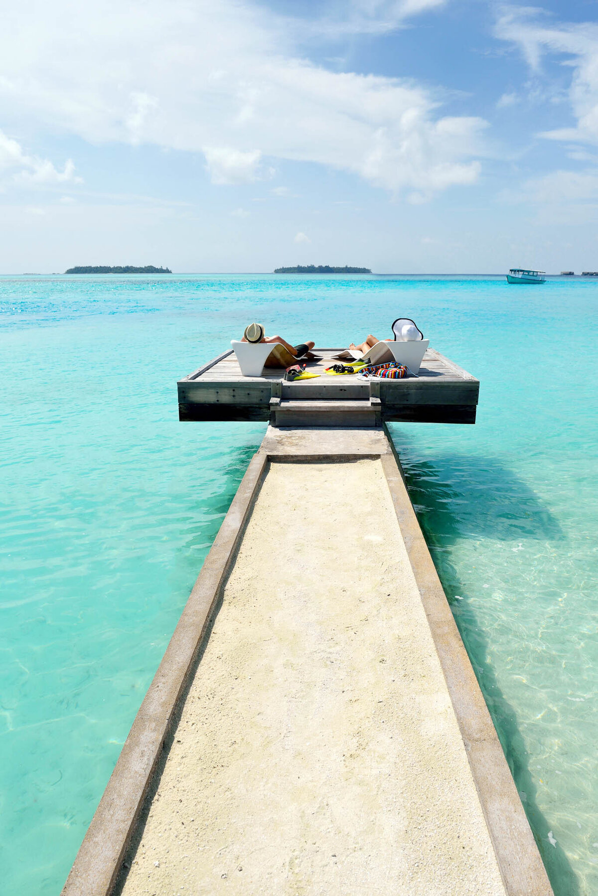 Couple relaxing on loungers at the end of a pier over turquoise water in the Maldives.