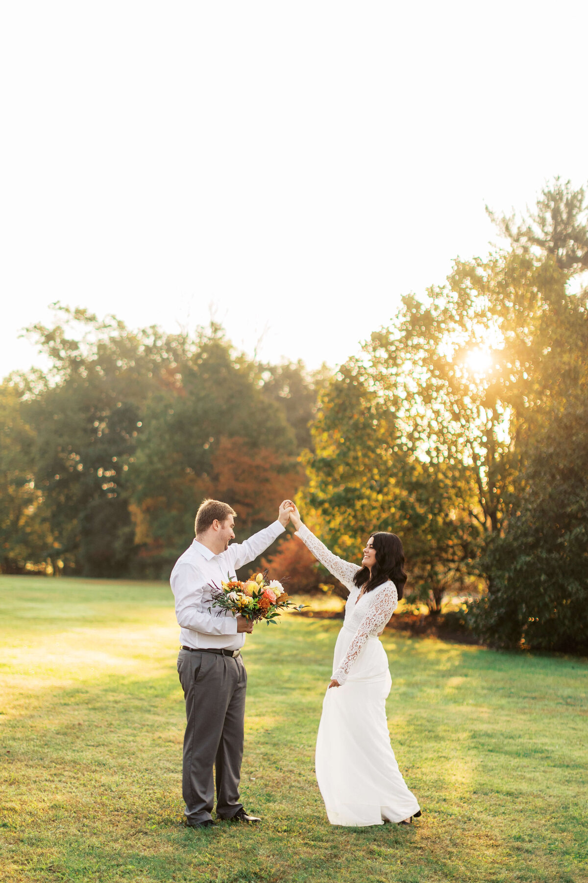 Groom to be holds his fiancee's bouquet while she twirls in a white dress.