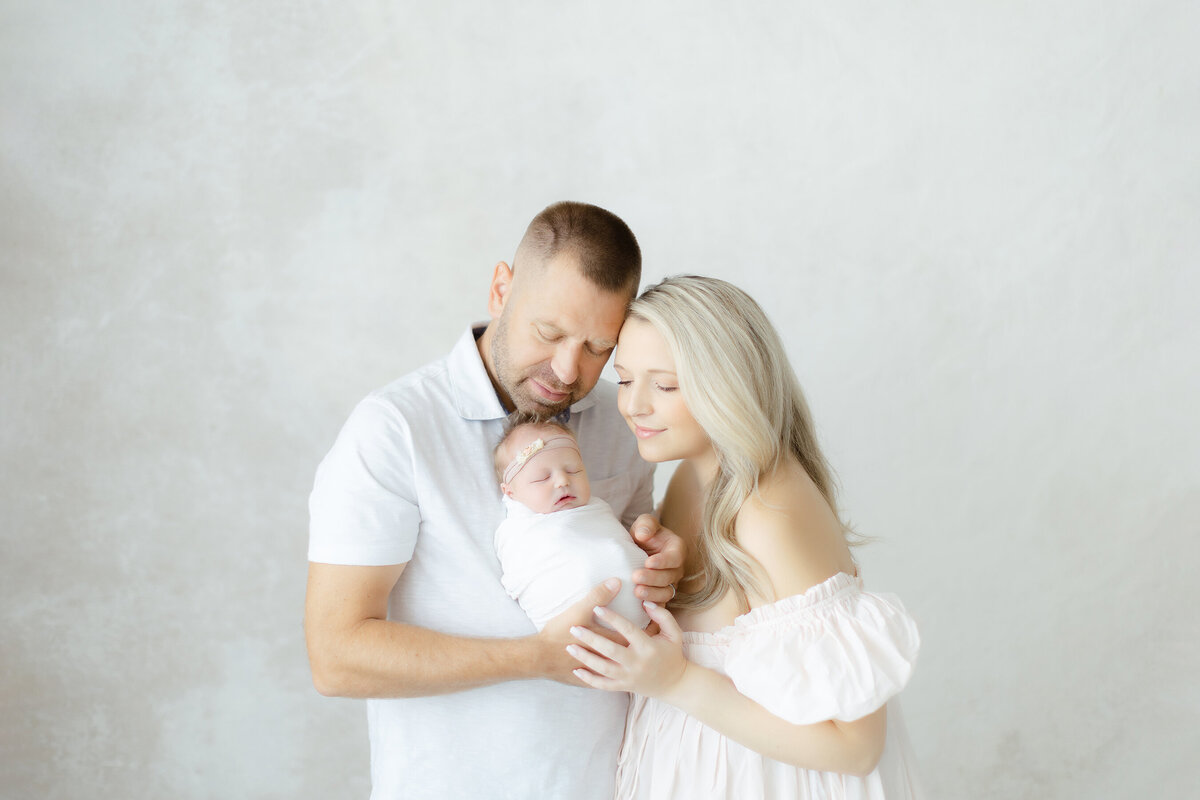 In studio newborn portrait of a mother and father holding their newborn baby girl close.