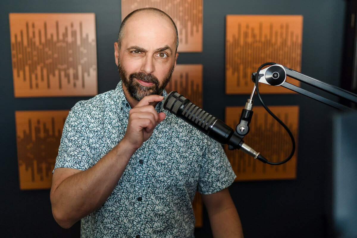 creative headshot of man tapping podcast mic with sound board in background
