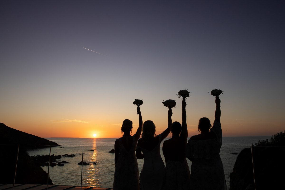 Silhouette of Bridesmaids with their flowers in the air at Tunnels Beaches wedding venue Devon