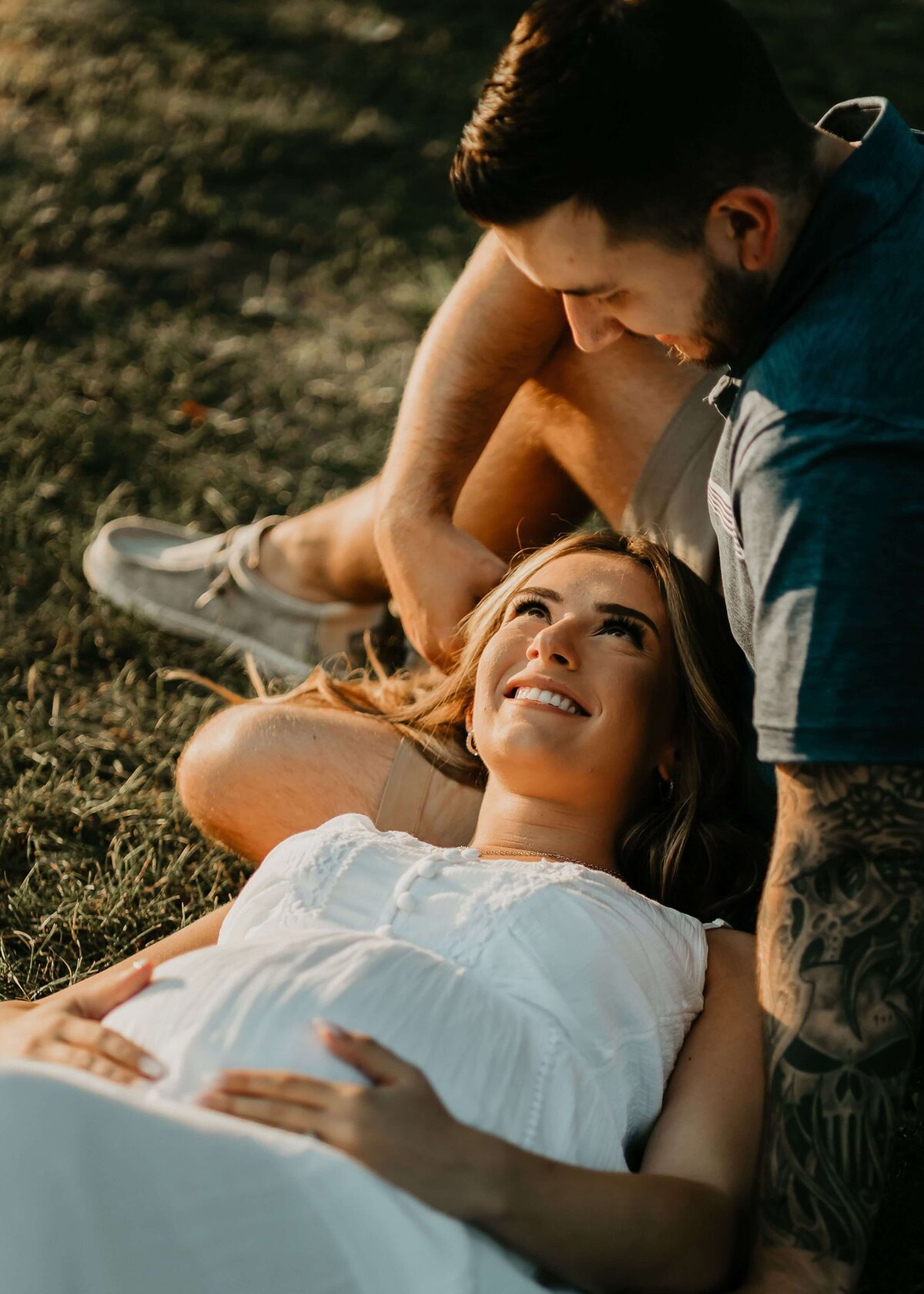 A pregnant woman and her husband lounging on the grass, captured by a Pittsburgh maternity photographer.