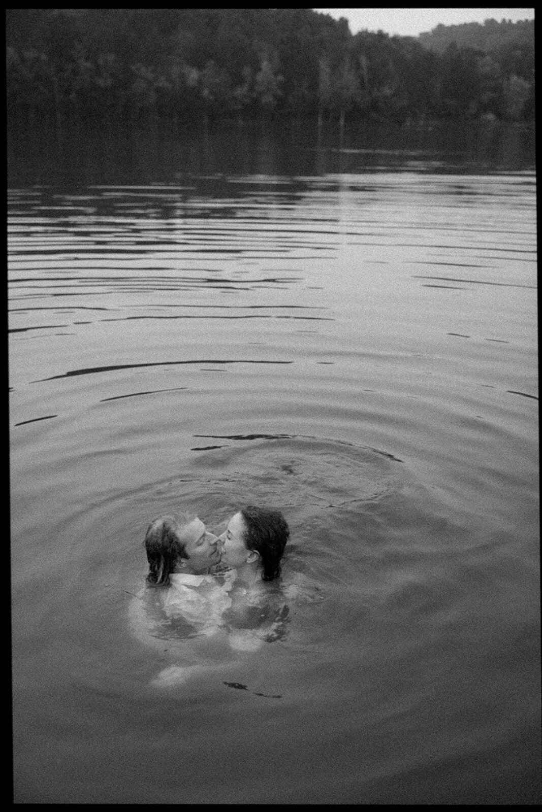 Couple treads water while kissing in a lake after they jumped in. 