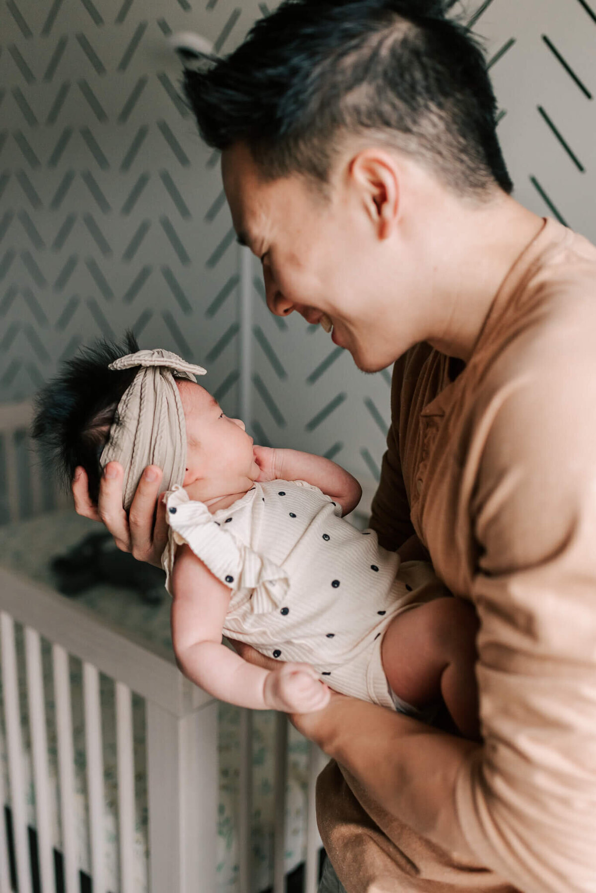 A dad smiling down happily at his new baby girl in their nursery