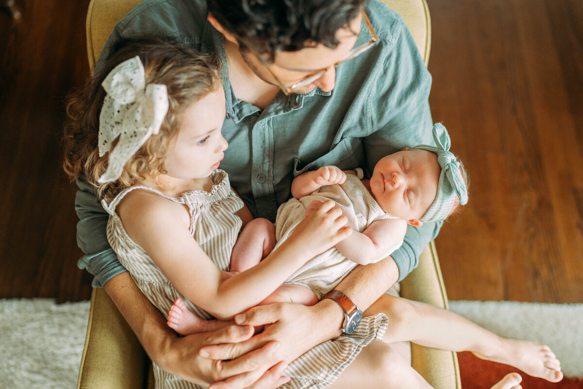 father holds baby and older sister in arms