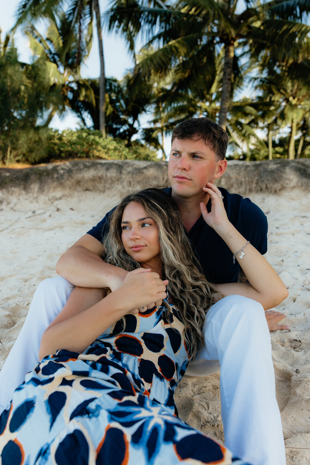 Candid shot of couple wrapped in each other’s arms with palm trees behind them at Kailua beach on Oahu