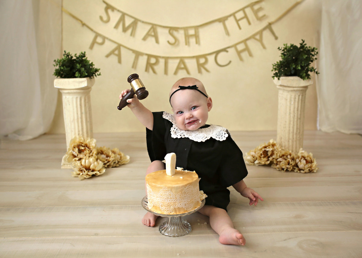 baby girl dressed as Ruth Bader Ginsberg with gavel and smash the patriarchy letting behind her