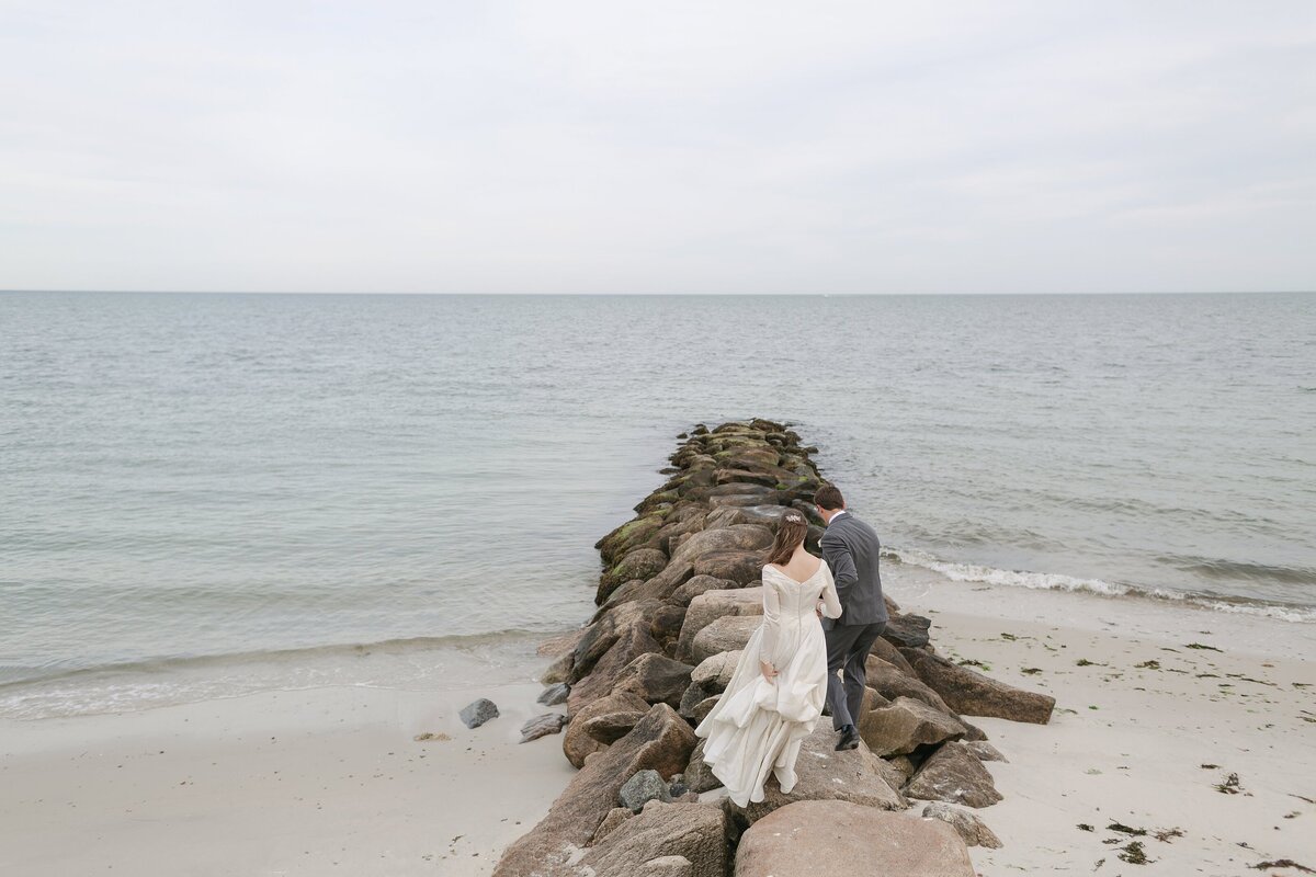 Bride and Groom walk out to a rock jetty at the Wianno Club.
