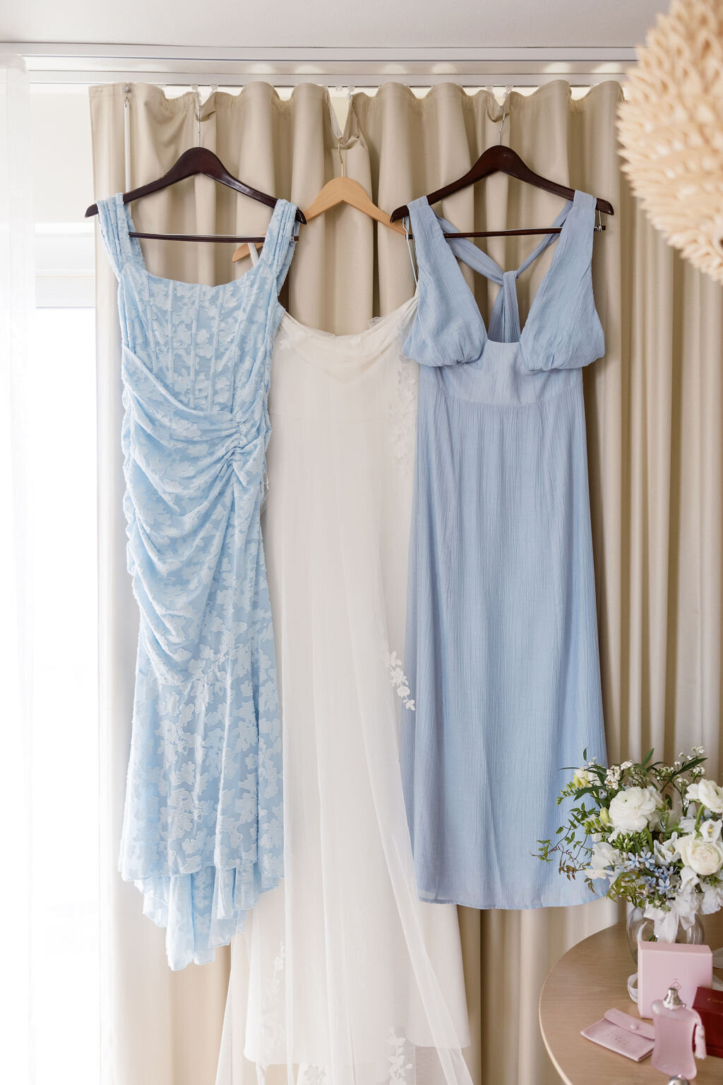 ivory crepe wedding dress hanging next to two baby blue bridesmaid dresses in hotel room
