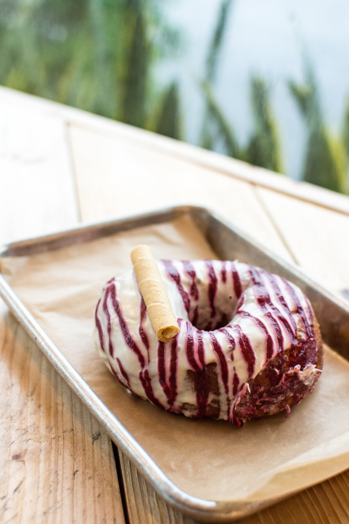 Red velvet donut with rolled wafer cookie on a parchment-lined tray with greenery in backrgound