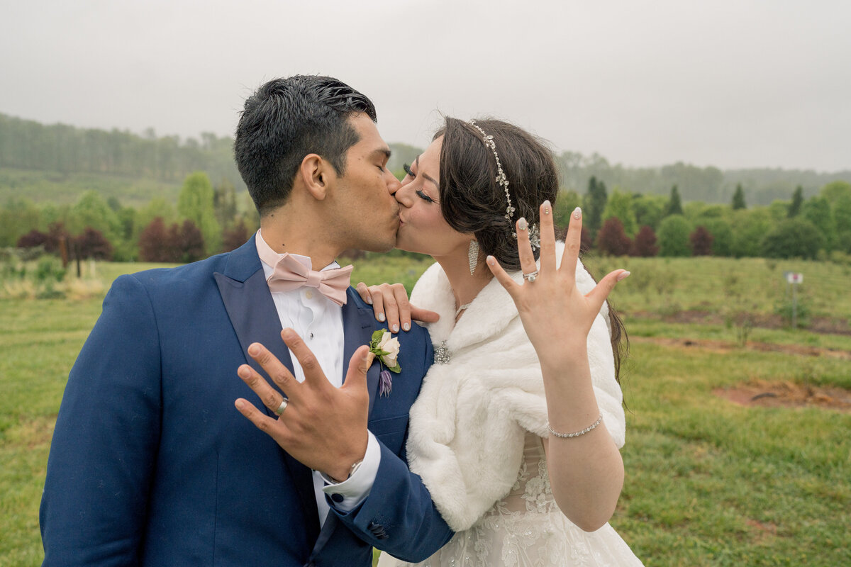 Bride and Groom kissing while showing off their brand new wedding ring in the mountains