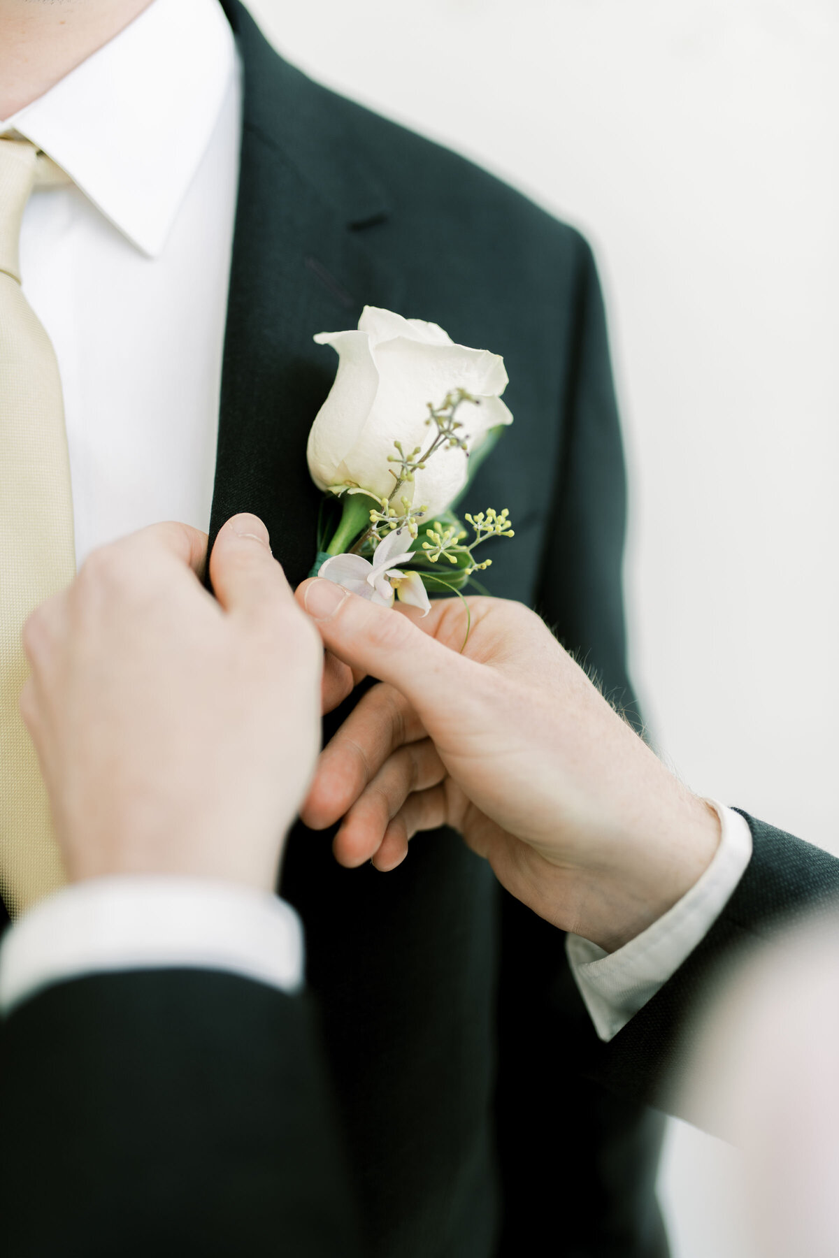 Groomsman helps groom with his boutonniere 