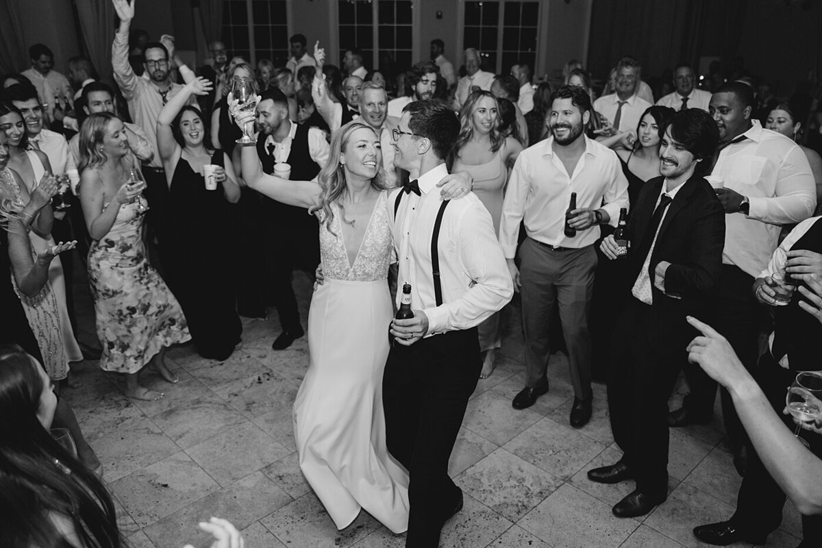 black and white reception photo of bride and groom dancing together surrounded by their wedding guests