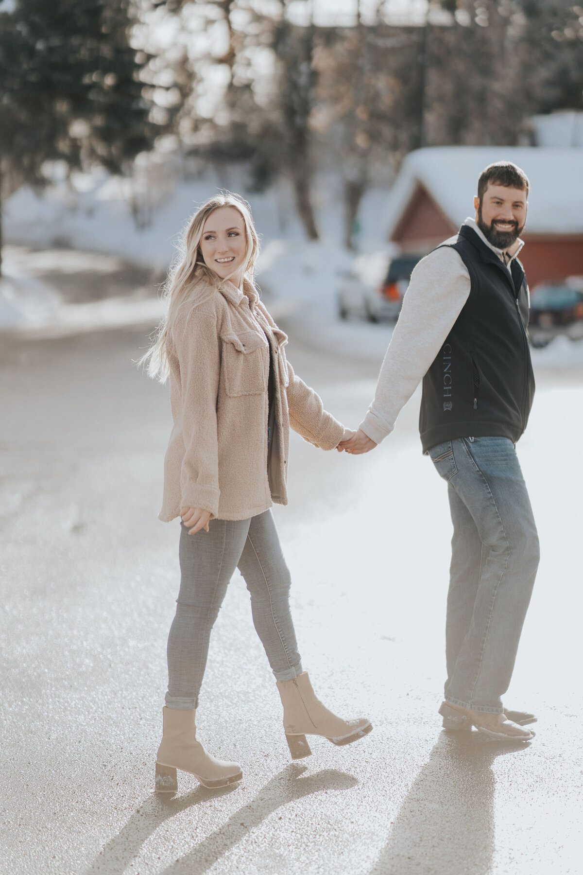 Engaged couple run through the streets of a small town while golden hues from the sun shine upon them captured by Idaho Falls Engagement Photographer