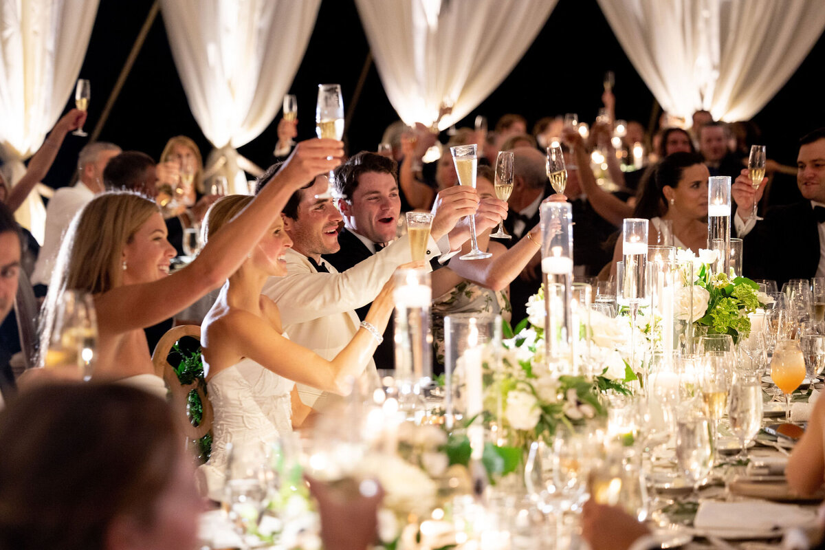 Table of wedding guests with glasses of champagne held in the air. 