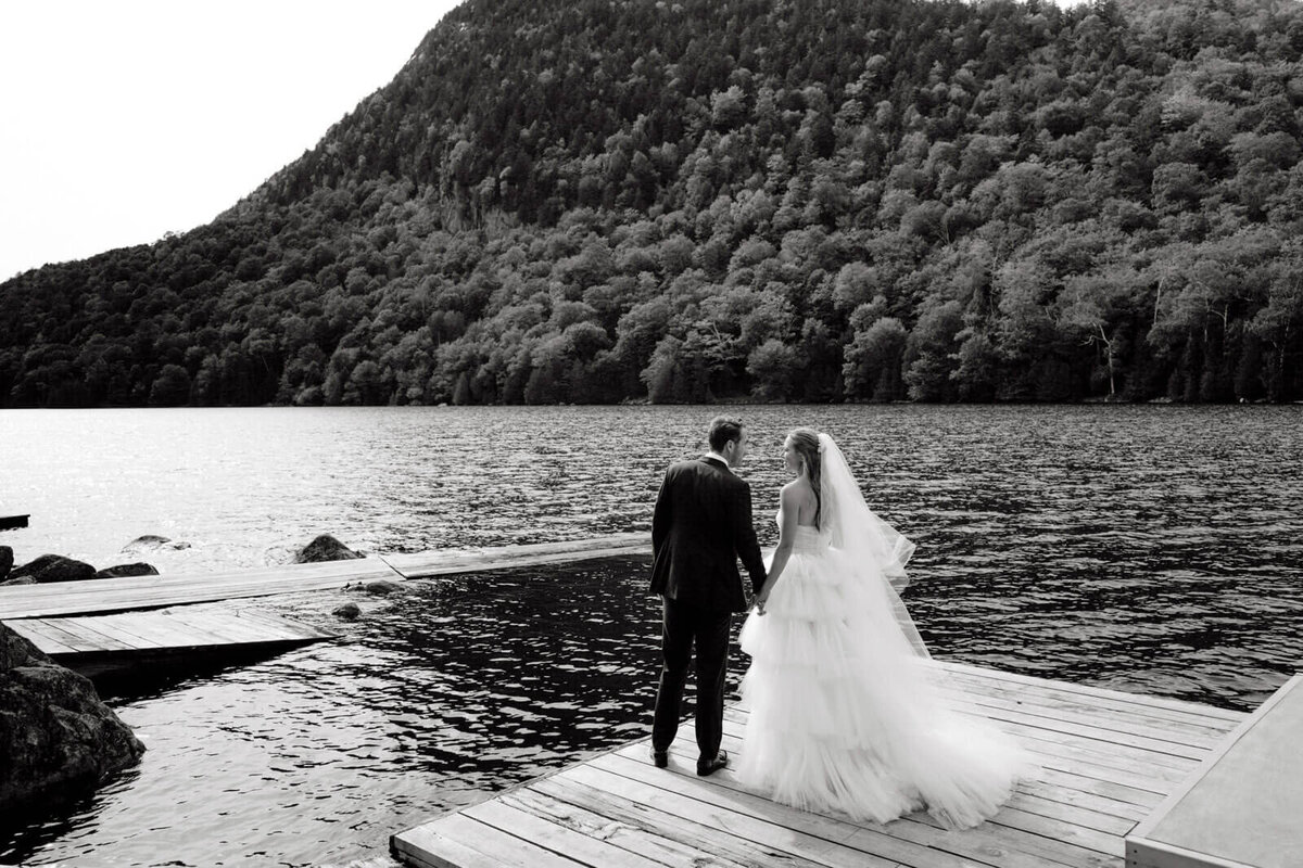 Black and white photo of the bride and the groom facing the mountains and sea on a wooden dock at The Ausable Club, New York.