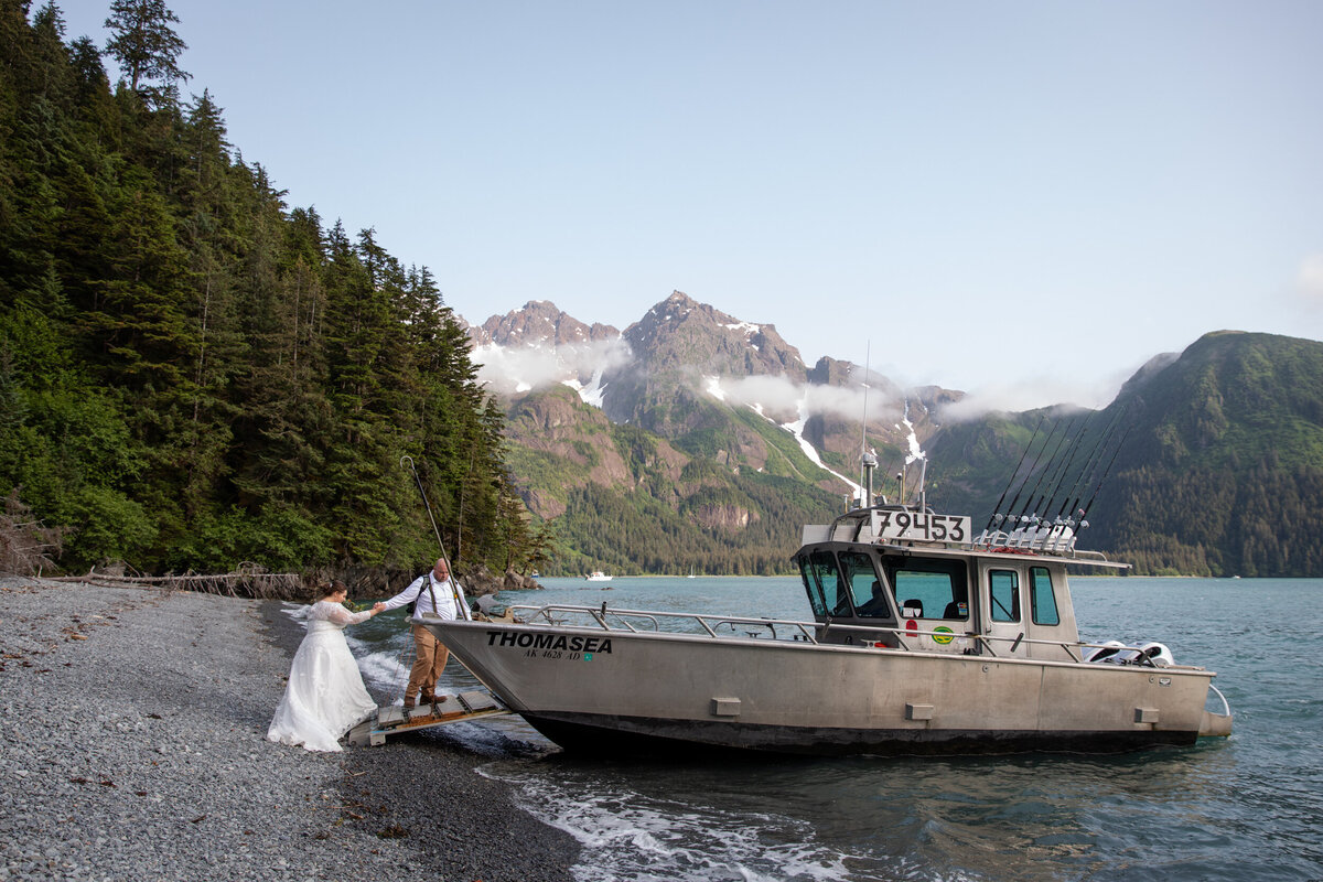 A groom helps his bride onto a boat in Alaska.