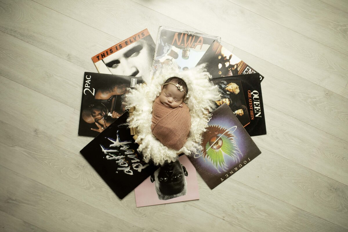 Newborn baby snugly wrapped and peacefully resting in the center of a collection of vinyl records, creating a unique and musical-themed portrait