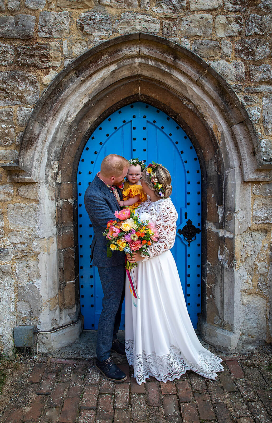 Bride, Groom and baby .  Post for photo by blue door of Bearsted Chuch
