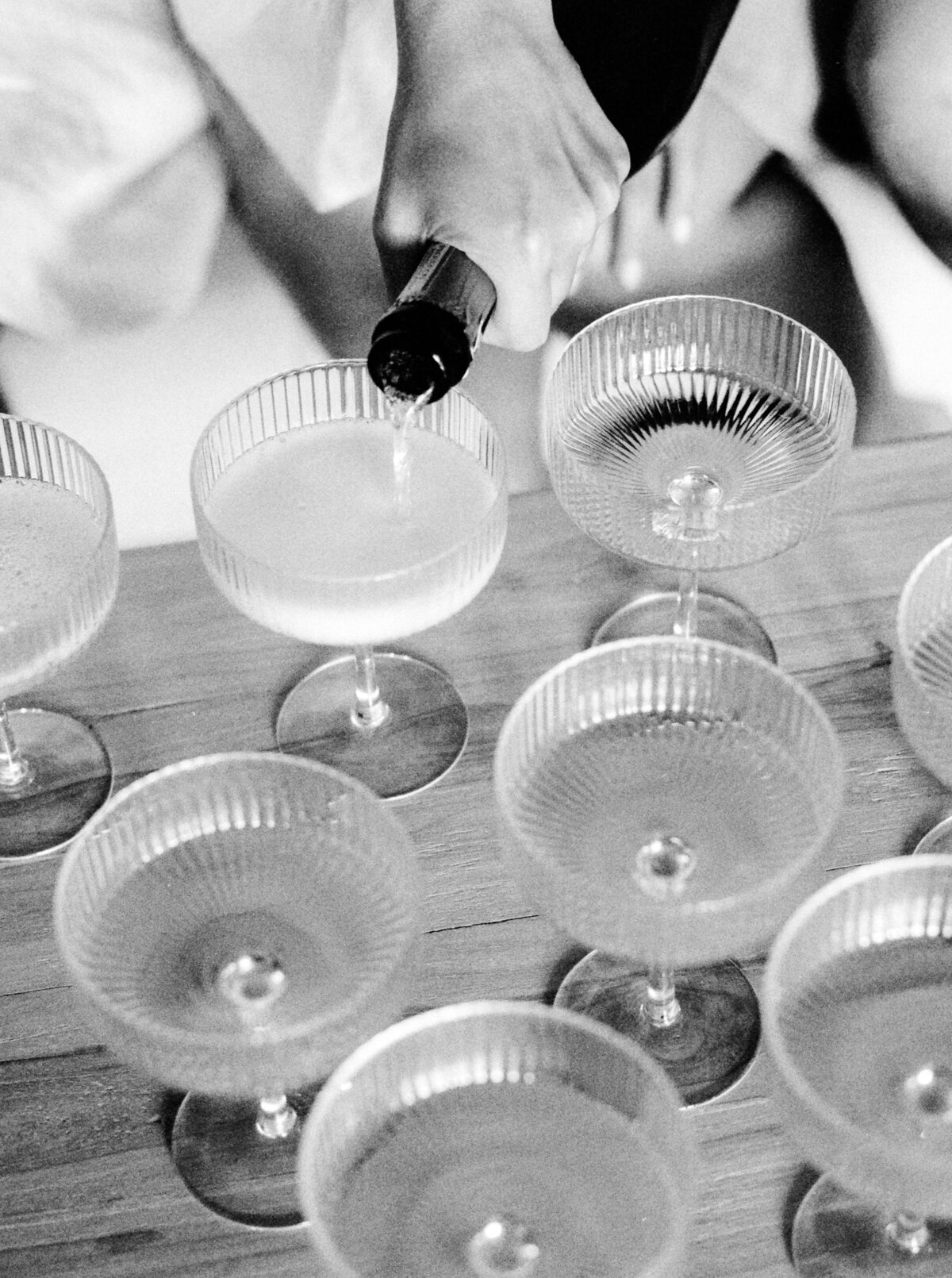 Black and white photograph of vintage champagne coupes being filled with champagne for bride and bridesmaids photographed by Italy wedding photographer at Villa Montanare Tuscany wedding