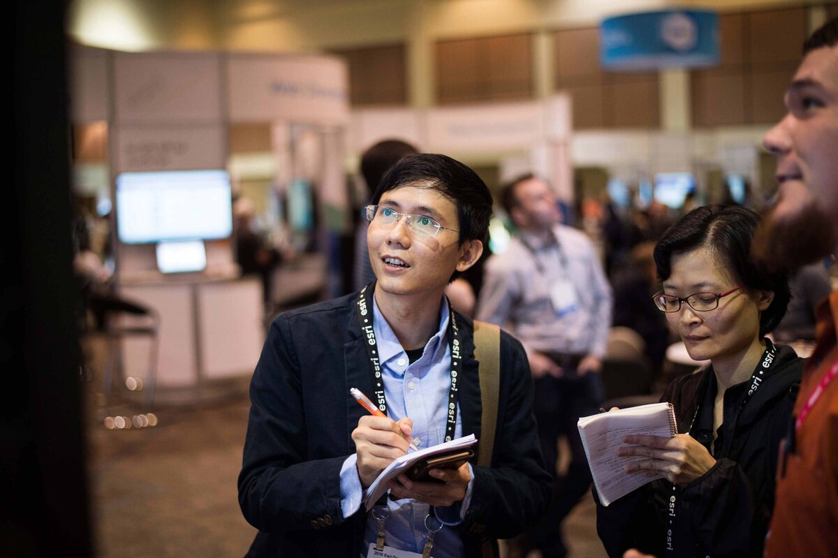 An asian man takes notes while standing at a booth at the ESRI annual conference