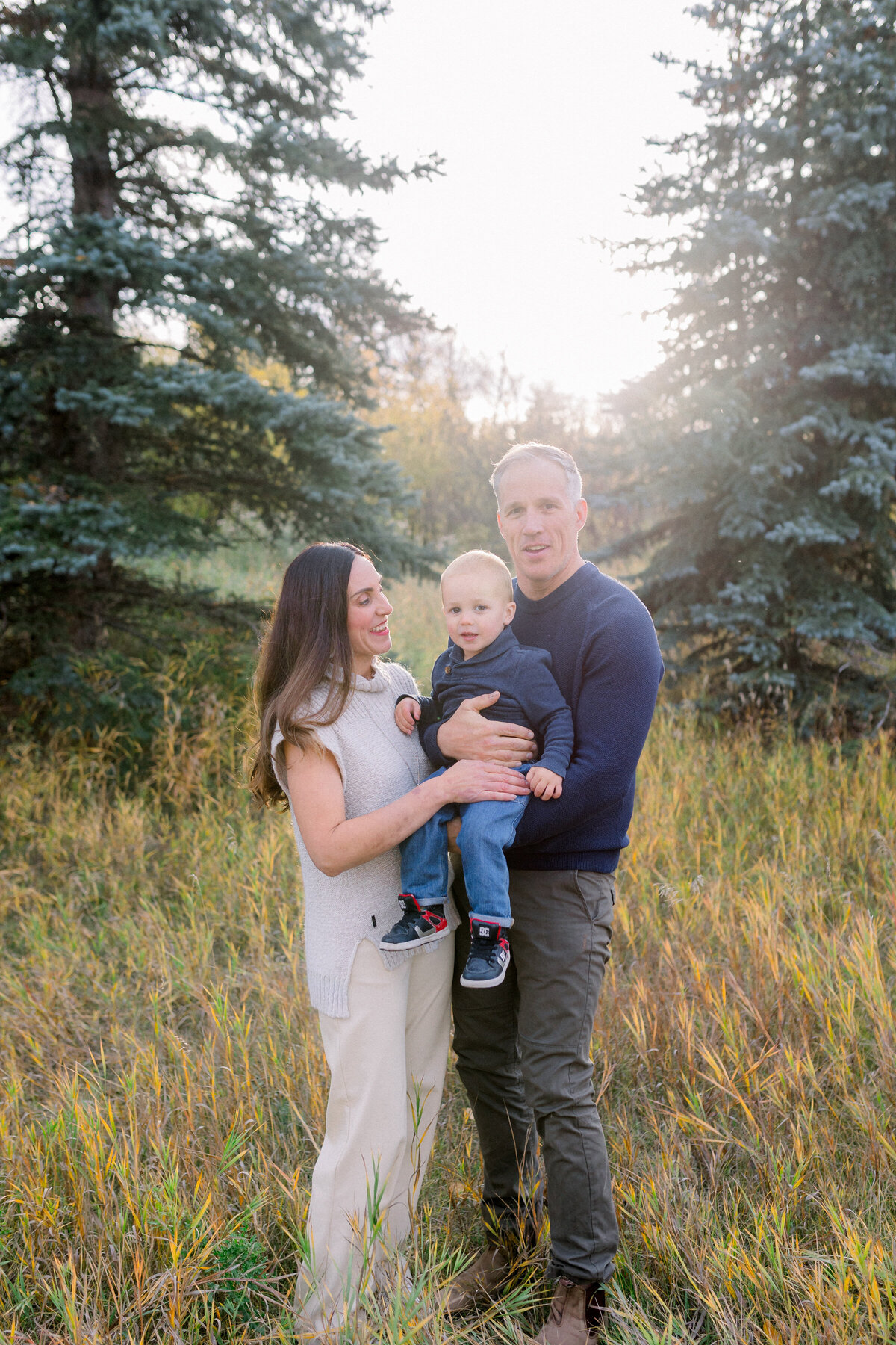 Mom and dad hold young boy at golden hour in a grassy park, Calgary, AB.