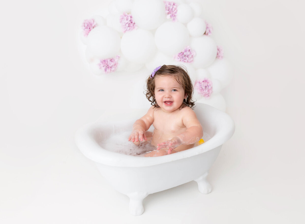 Baby girl sitting in a white bath lilac and white cake smash 1st birthday photoshoot in NYC 