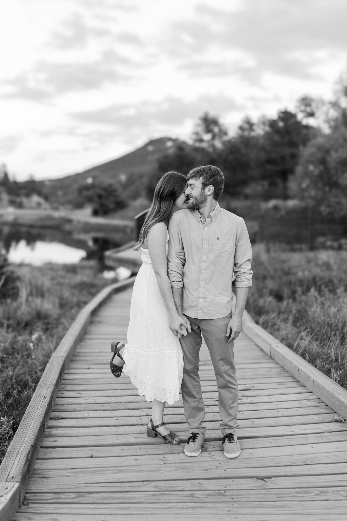 summer engagement photos on a dock in the mountains of colorado. the bride is hugging her fiance from behind