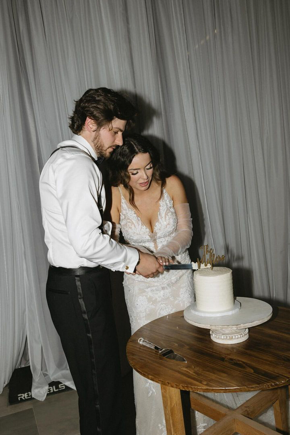 Couple cutting white wedding cake with floral accents by Sweets By Sue in Lethbridge, Alberta, featured on the Brontë Bride Vendor Guide.