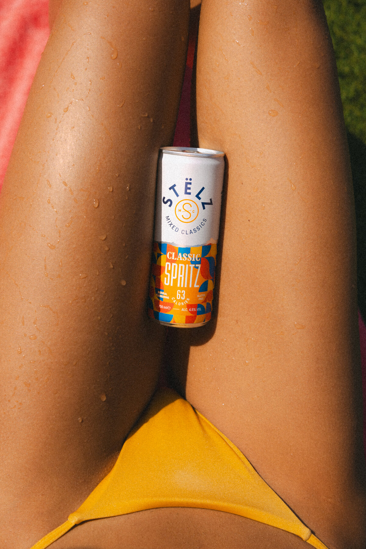 A can of STËLZ Classic Spritz rests on the legs of a woman lying in the sun, droplets of water glistening on her skin. The image captures a moment of pure relaxation and refreshment. Photography by Bo Eppink.
