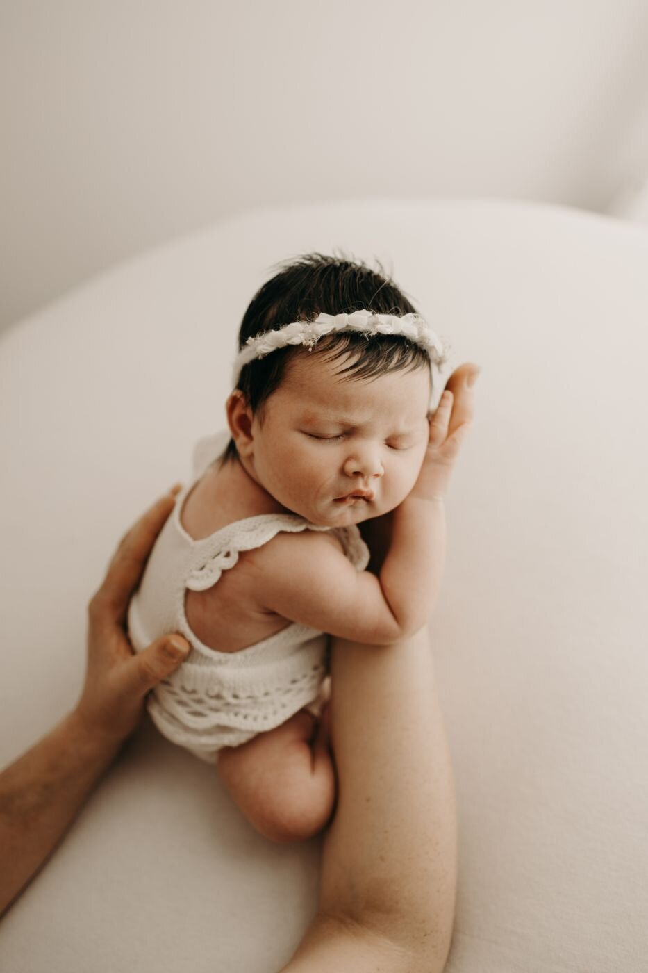 Serene portrait of a sleeping newborn with dark hair and a textured headband, being carefully posed by a Mullingar newborn photographer