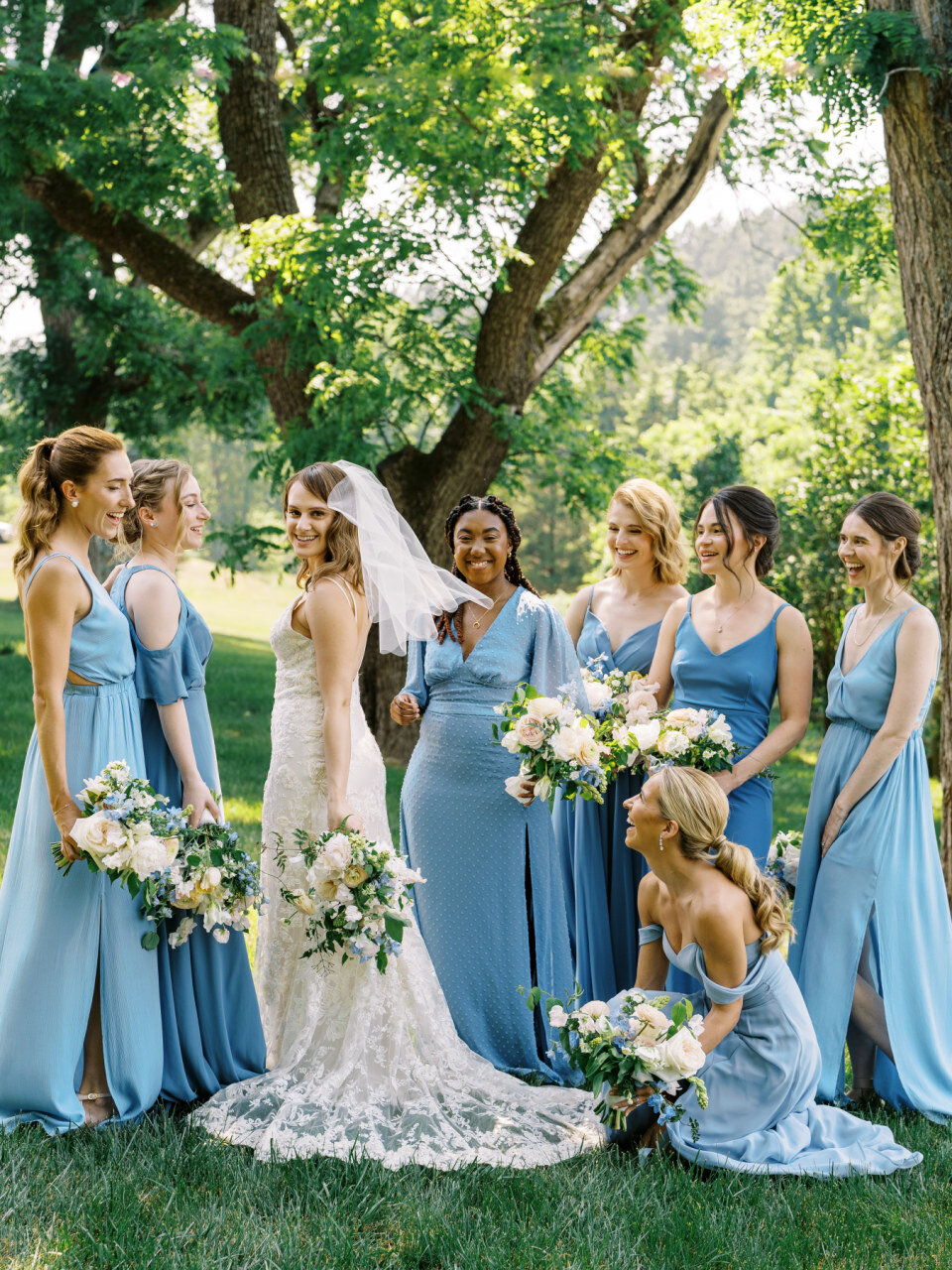 Seven bridesmaids wearing blue dresses surrounding a bride wearing a white dress and veil