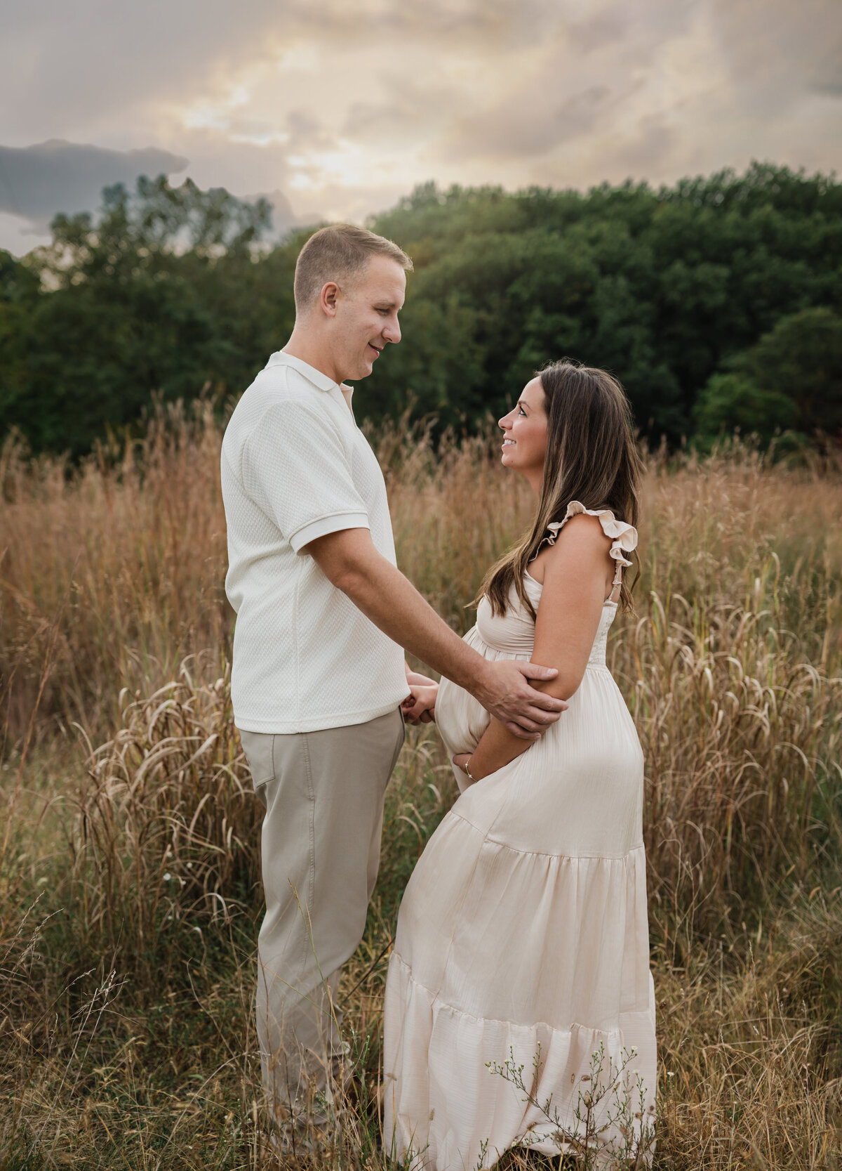 husband and pregnant wife in pink silk maternity gown holding baby bump for maternity photoshoot