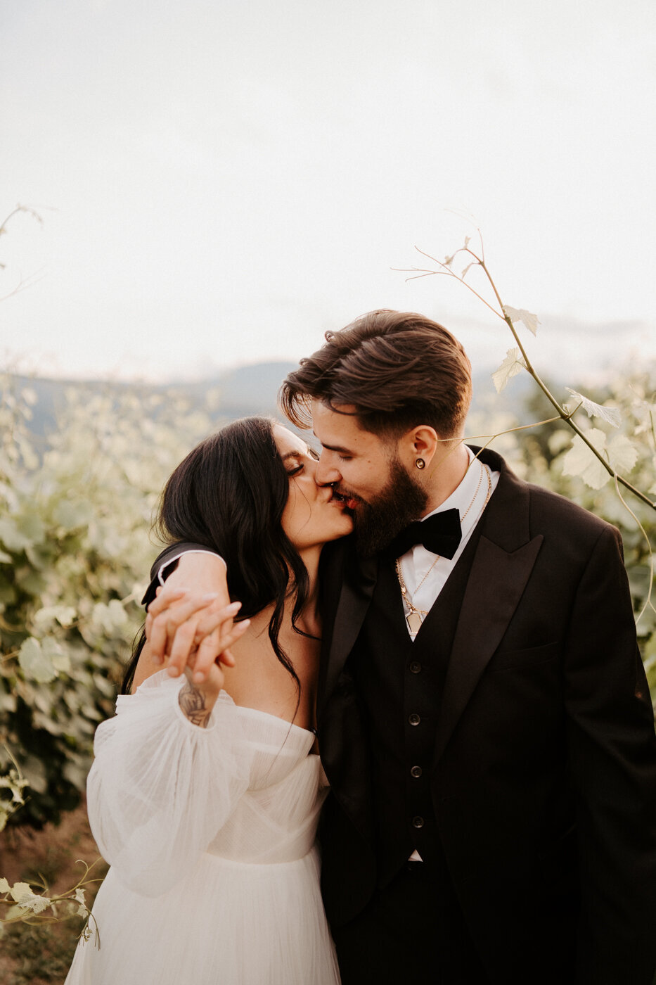 Kelowna Wedding Couple over looking the Okanagan Lake in Lake Country BC.  They are wearing modern sleek wedding attire with a gorgeous wedding dress and black tux.  A huge floral arch behind them filled with babysbreath.  A modern wedding day with a gorgeous look out!  They are dancing in their reception at the 50th Parallel Estate