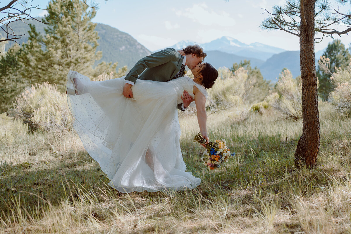 Groom dips bride for kiss in mountain forest