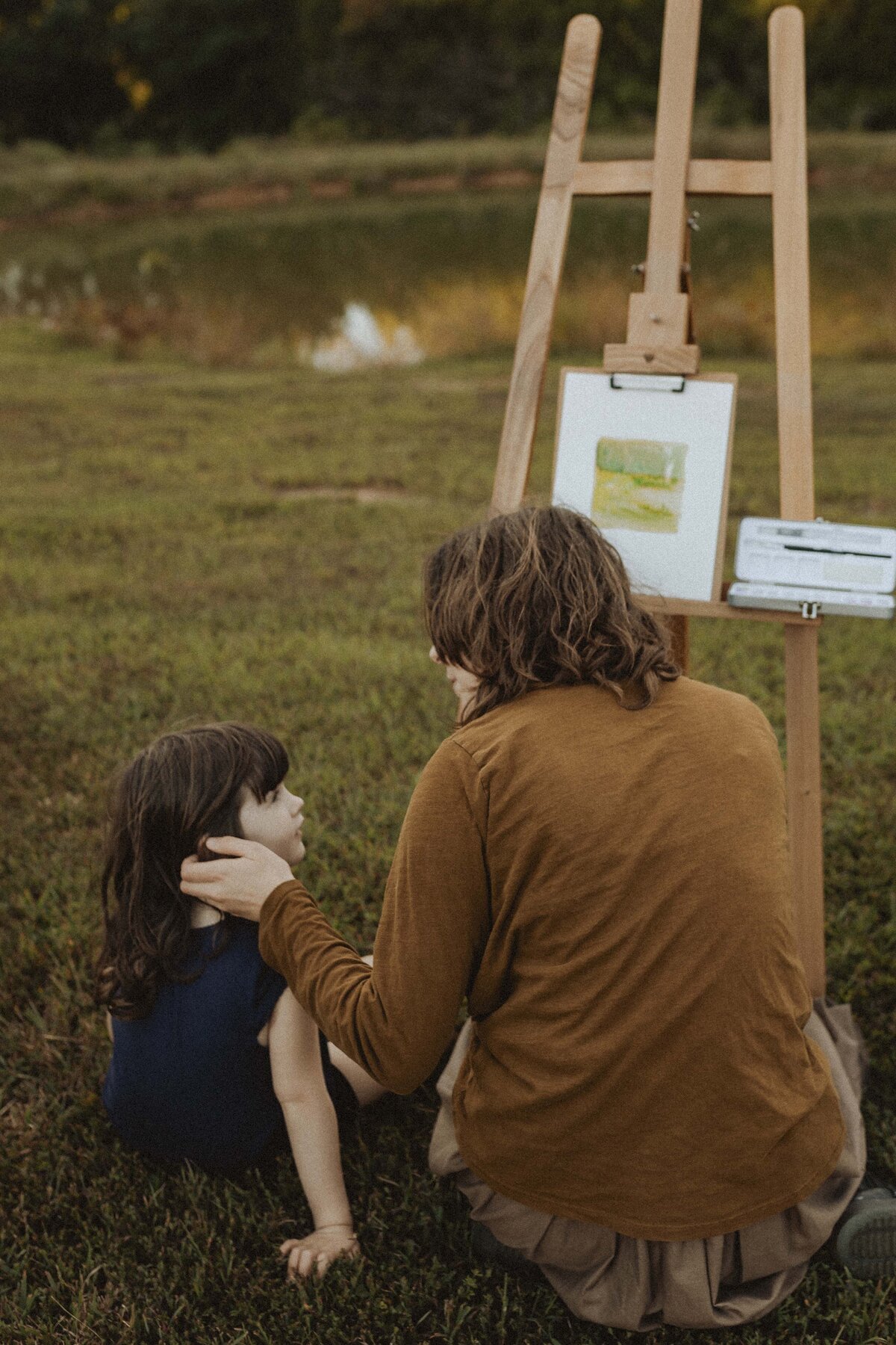 Mother and daughter share sentimental moment by pond as mother paints with cinematic feel