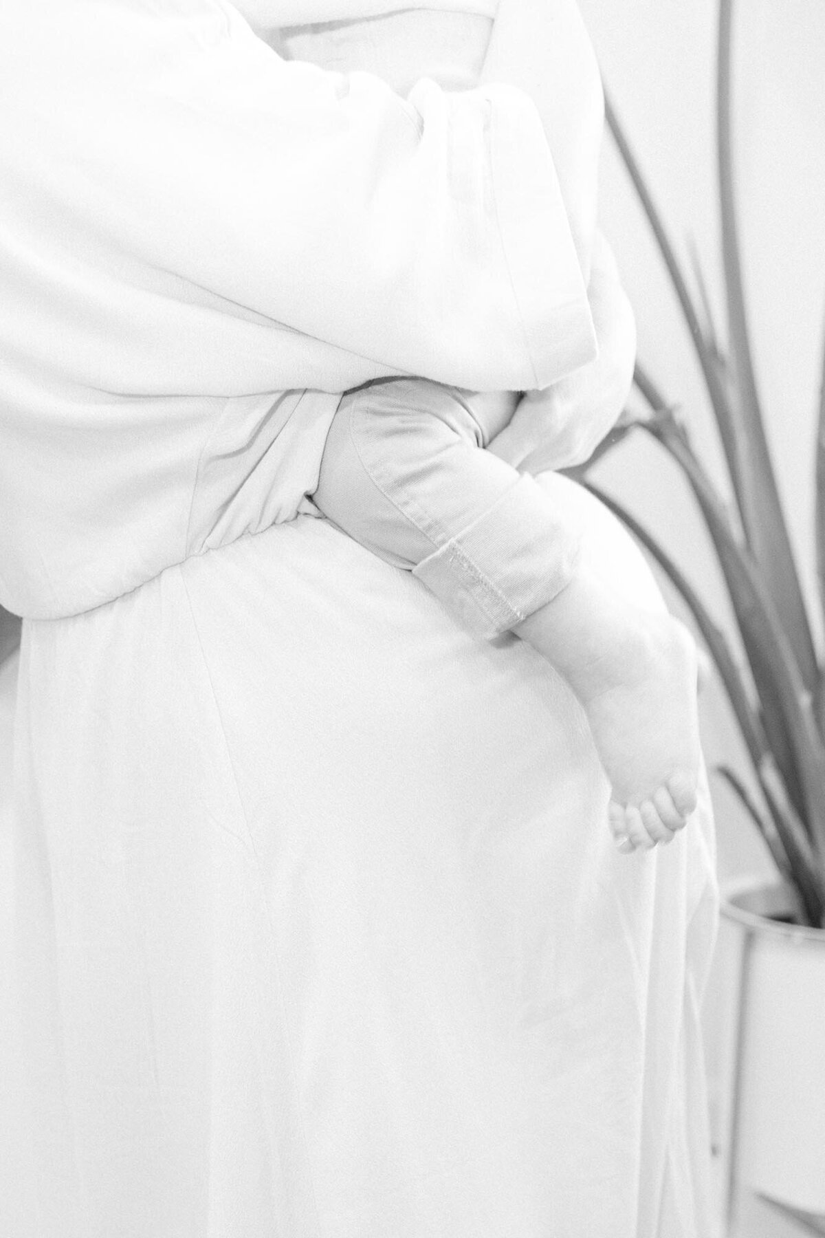 a close up black and whit photo of a pregnant woman holding her toddler with his feet hanging over her belly