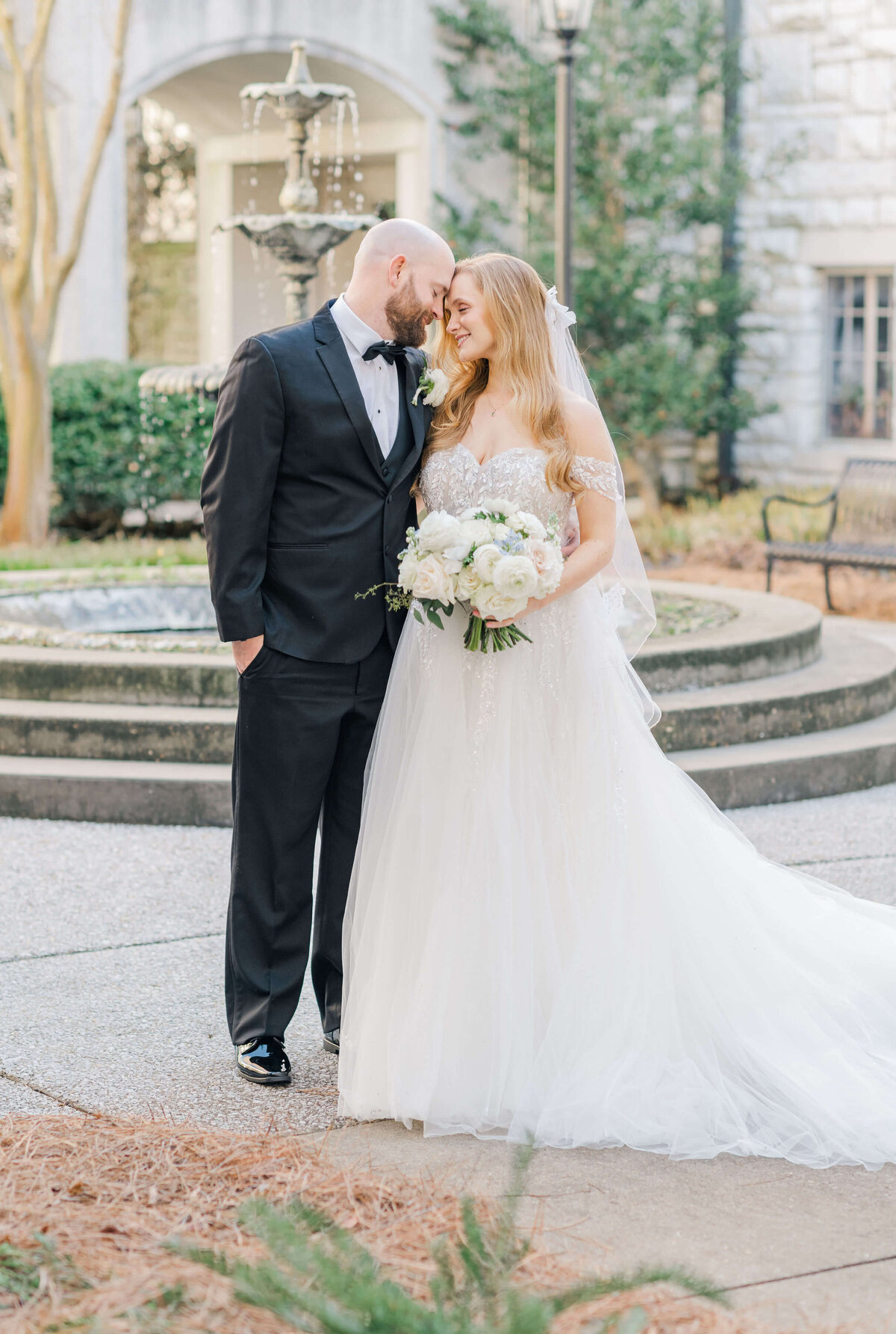 Bride and groom standing together in a courtyard with foreheads touching and smiling