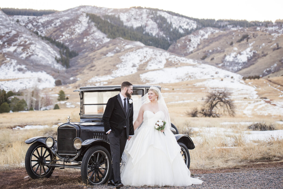 A bride and groom stand hand-in-hand in front of the vintage stagecoach car at The Manor House in Littleton, Colorado.