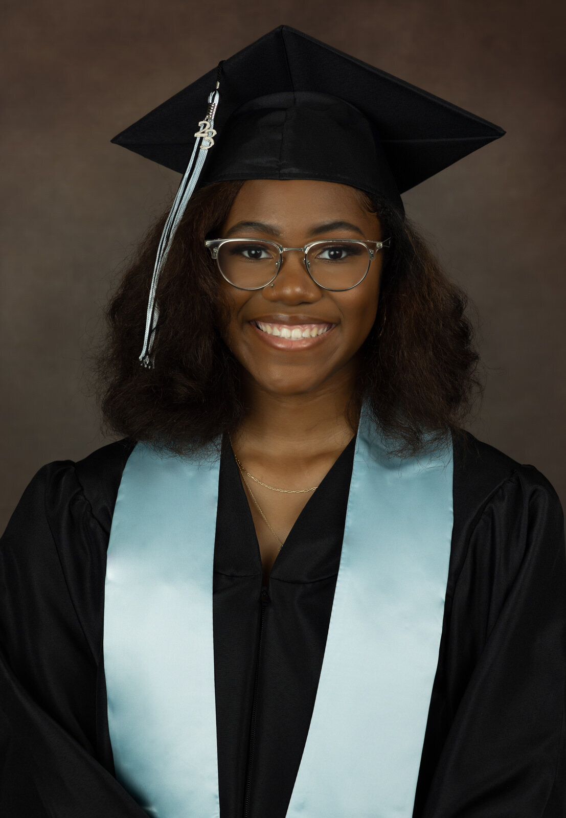 senior-girl-in-cap-and-gown-with-brown-backdrop