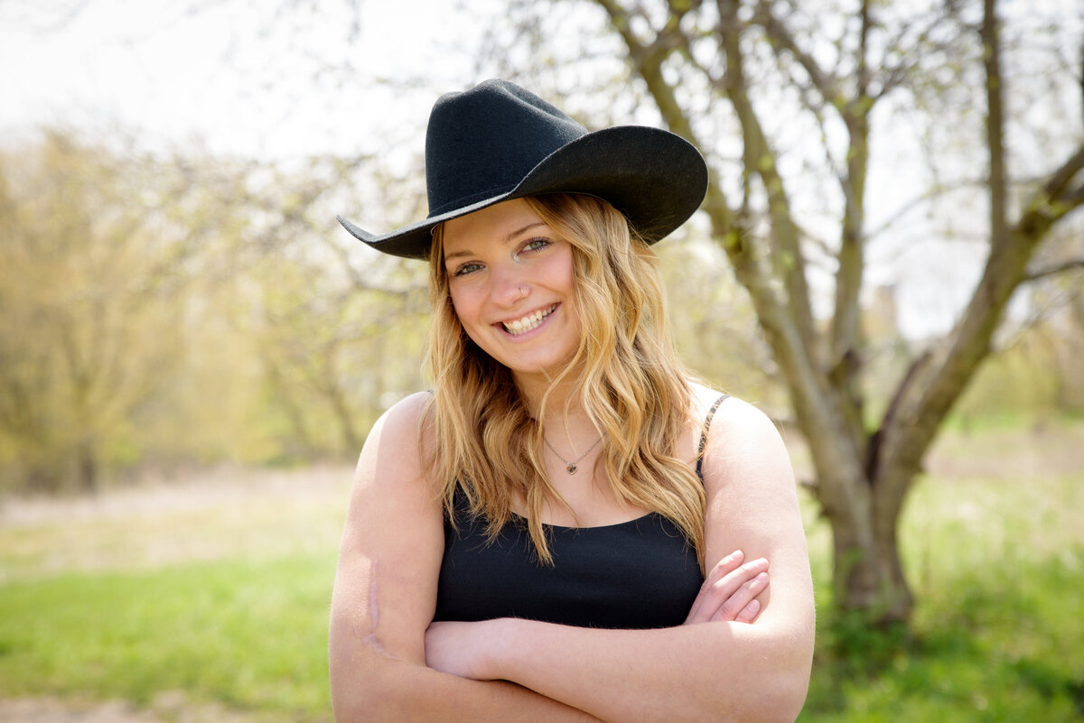 High school senior girl standing in field at Fonferek Glen County Park in Green Bay, Wi wearing cowboy hat and dress.