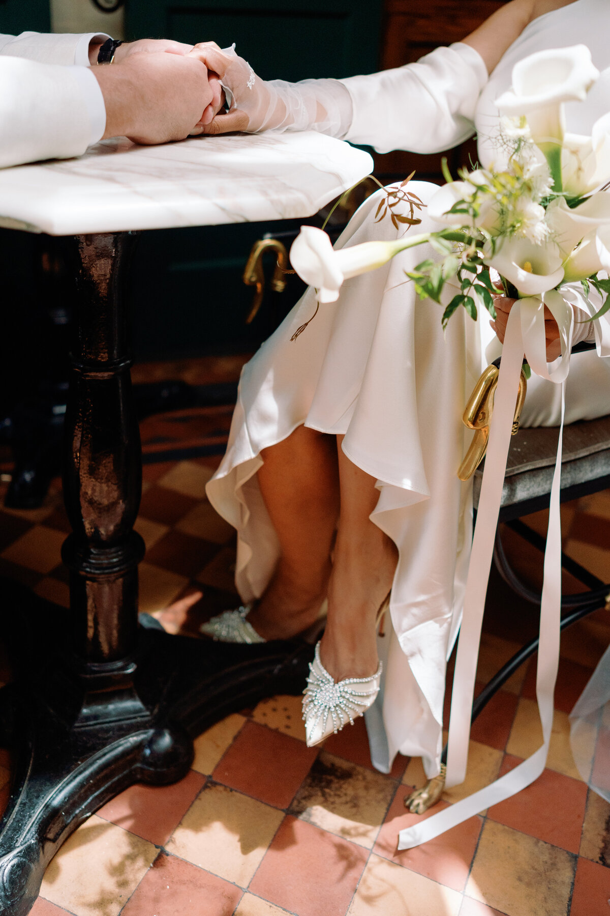 Close-up of the bride’s jeweled heels and bouquet while seated inside Hotel Chelsea during Japna and Chris’s New York City elopement, photographed by NYC wedding photographer Perry Hancock.