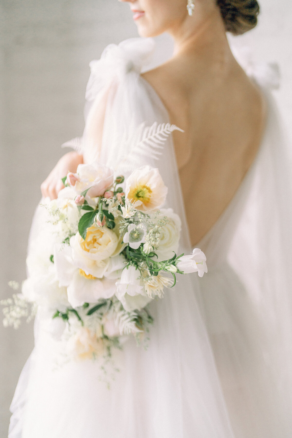 a bride with her back to the camera looking away with her bouquet on her side and in focus