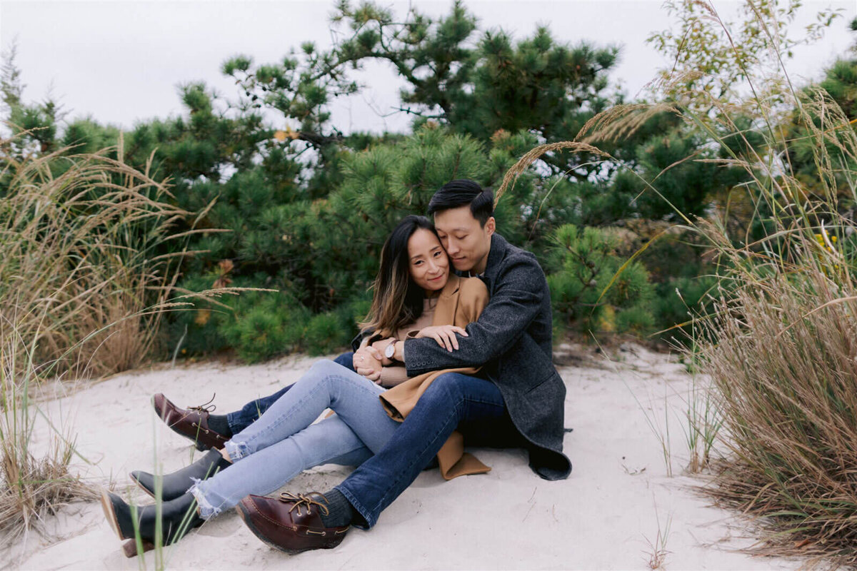 The engaged couple is romantically sitting on the white sand in Fire Island Beach, New York. Engagement Image by Jenny Fu Studio