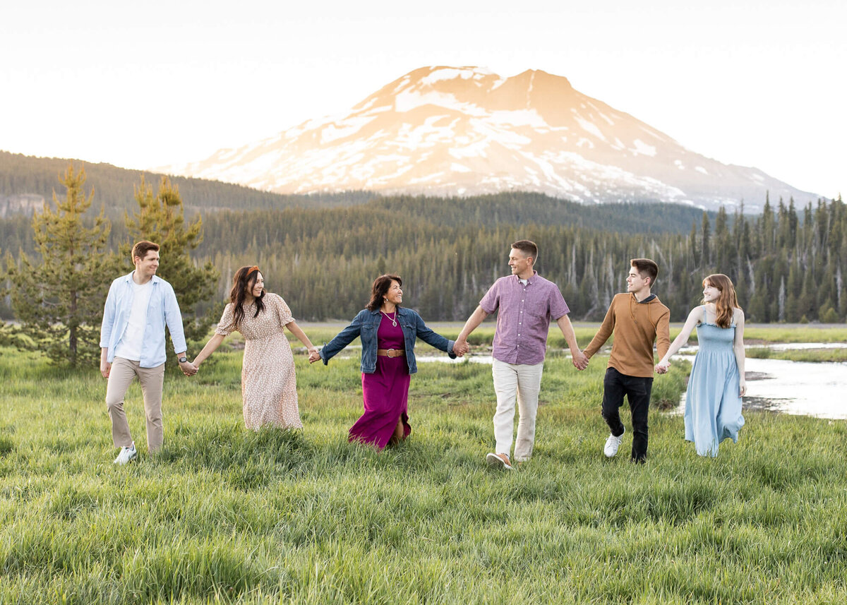 A family of six holding hands walking in a beautiful meadow in front of South Sister in Oregon by Oregon photographer Jaime Bugbee