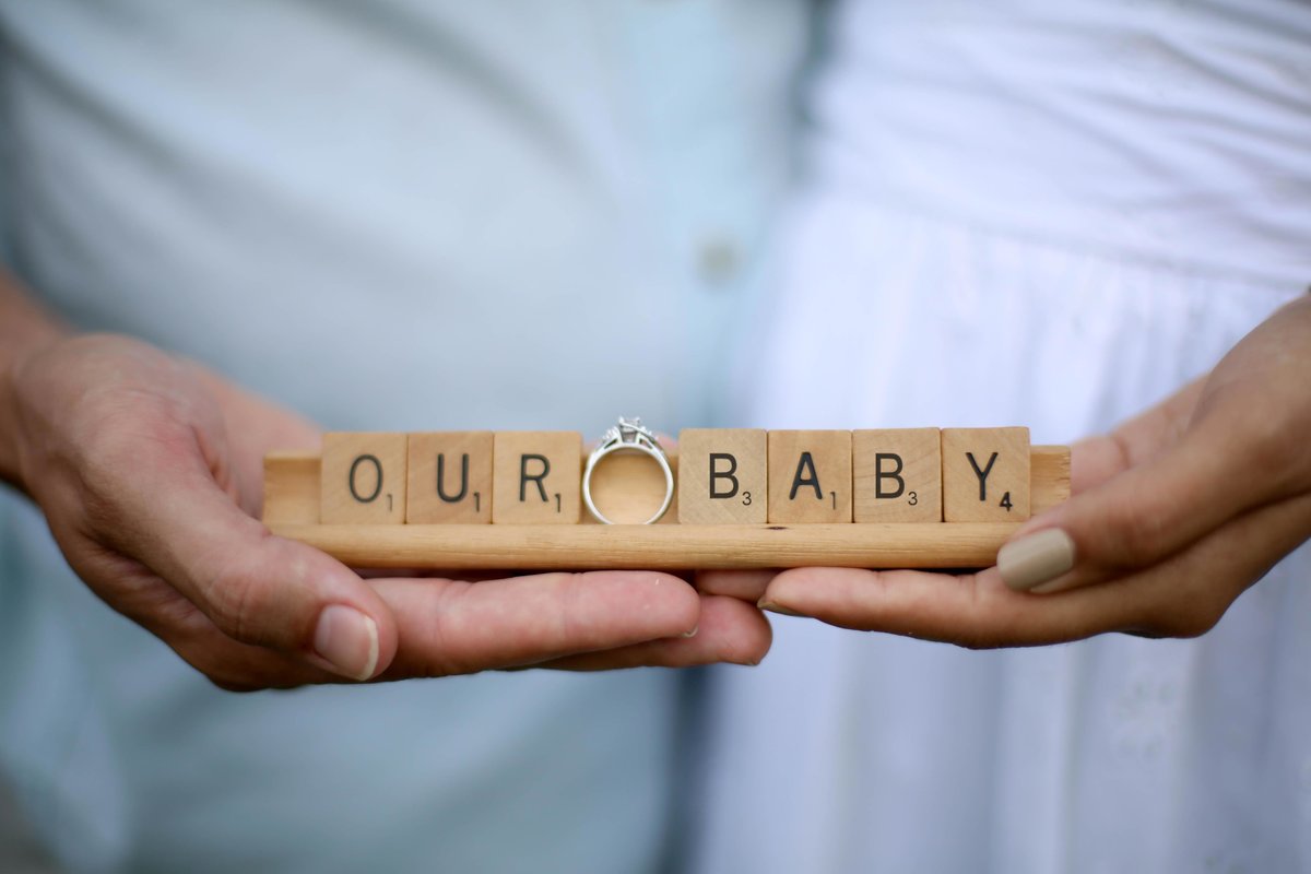 Hands holding scrabble tiles spelling "our baby" with a wedding ring. Photo by Ross Photography, Trinidad, W.I..