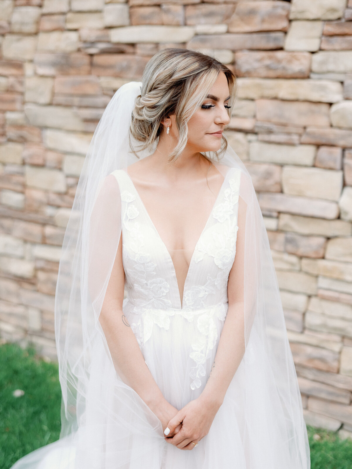 A bridal portrait of a bride wearing a lace deep v-neck wedding dress and tool veil as she looks over her shoulder and holds her hands in front of her body