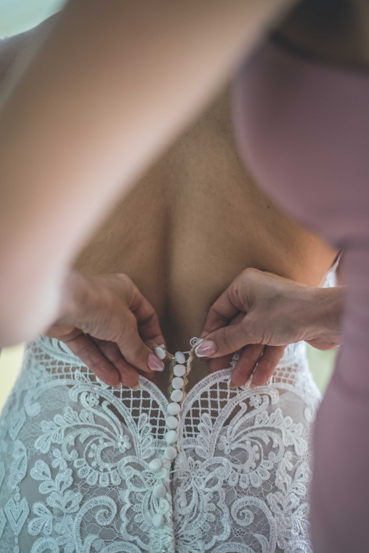 a bride getting her dress buttoned from the back